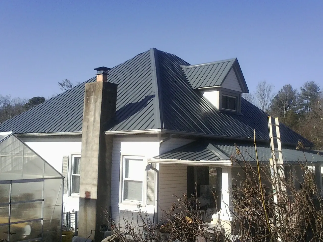 Dark blue standing seam metal roof on a white farmhouse with dormer — Slate & Tile Roof Repair by Roofing Brothers in Cokeburg