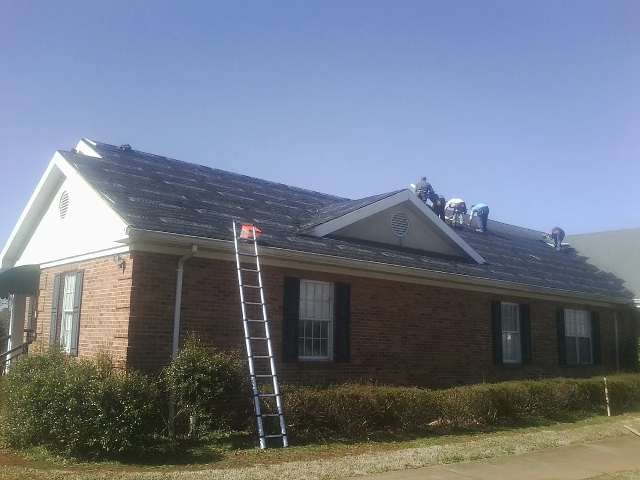Crew tearing shingles off a brick ranch roof with a ladder set — Emergency Roof Repair work by our crew in Cokeburg