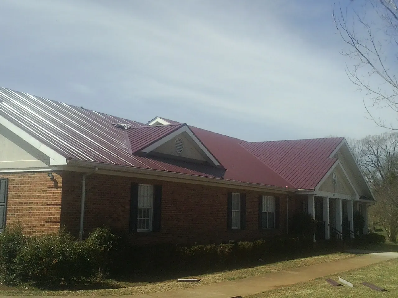 Red metal roof with gabled entries on a long brick building, from a Hail Damage Roof Repair job in Cokeburg