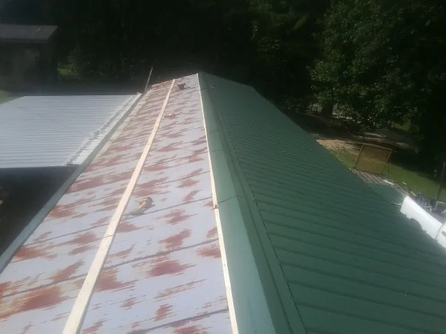 Old rusted panels beside newly installed green metal roofing — Wind Damage Roof Repair by Roofing Brothers in Cokeburg