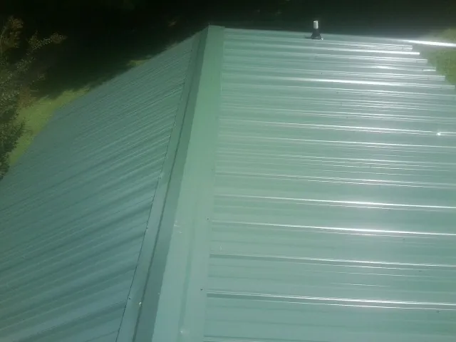 New green metal panels meeting at the ridge of a roof — Flat Roof Repair work by our crew in Cokeburg