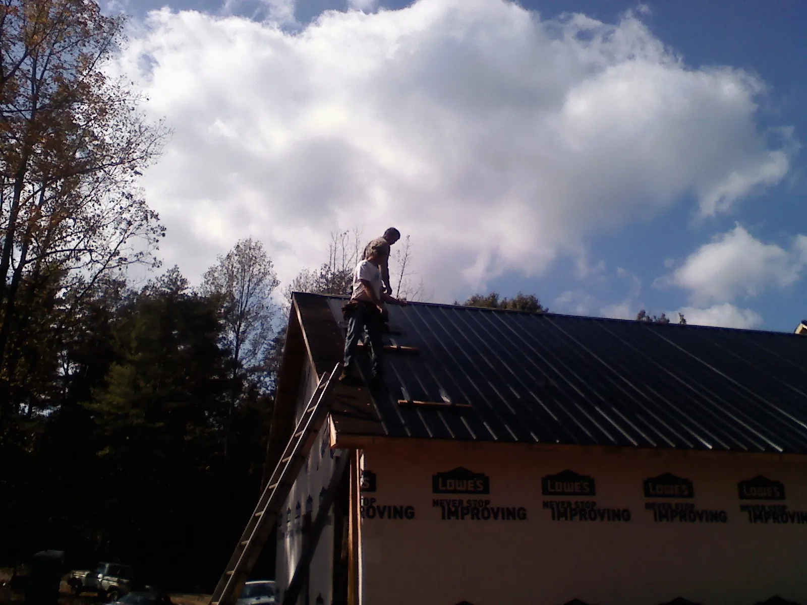 Roofer fastening dark metal panels high against a cloudy sky, from a Roof Inspection job in Cokeburg