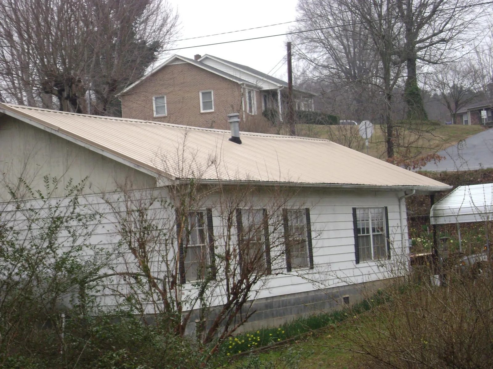 Tan metal roof on a white sided house set into a hillside — Commercial Roofing by Roofing Brothers in Cokeburg